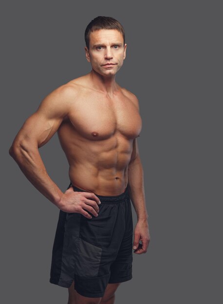 Мускулистый загорелый мужчина среднего возраста без рубашки изолирован на сером фоне.