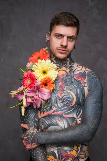 Shirtless tattooed hipster young man with flower on his body and piercing in his ears and nose looking at camera