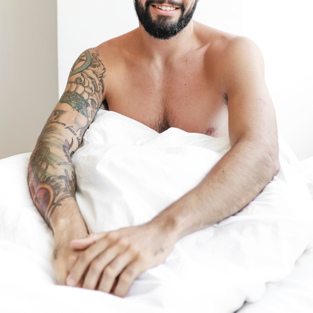 Free photo shirtless young man sitting on bed