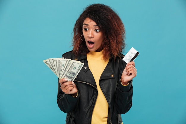 クレジットカードを保持している革のジャケットでショックを受けたアフリカ人女性