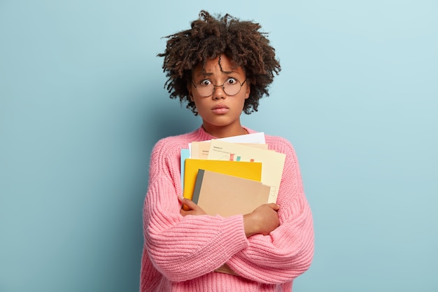 Shocked Afro American university student stands with textbooks, afraids of passing exam