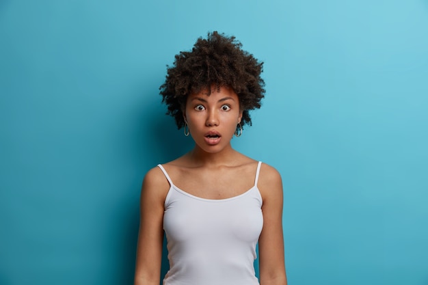 Free photo shocked afro american woman in casual wear, drops jaw from amazement, stands speechless and looks in disbelief, stares big eyes,