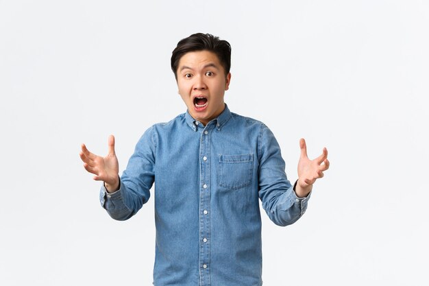 Shocked and alarmed asian man reacting to terrible news, standing in panic over white background and shaking hands indecisive, dont know what do, feeling useless, white background.