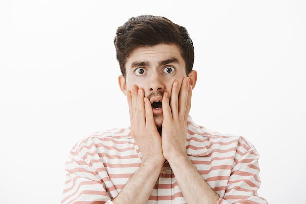 Free photo shocked and anxious handsome male model with moustache, touching cheeks with hands nervously, dropping jaw and staring, being stunned with disappointing rumor or news