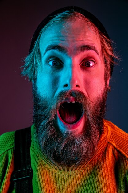 Shocked, astonished, close up. Caucasian man's portrait on gradient studio background in neon light. Beautiful male model with hipster style. Concept of human emotions, facial expression, sales, ad.