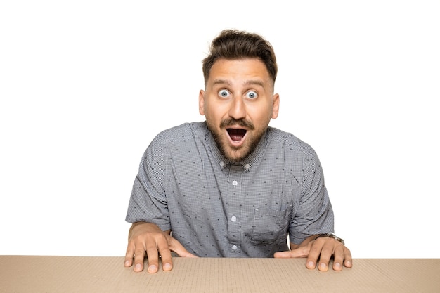 Free photo shocked and astonished man opening the biggest postal package. excited young male model on top of cardboard box looking inside.