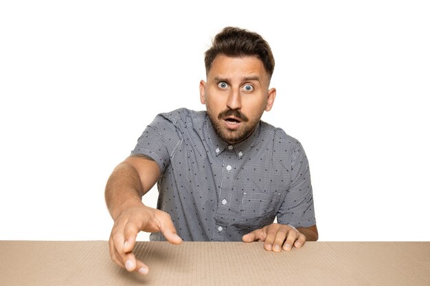 Free photo shocked and astonished man opening the biggest postal package. excited young male model on top of cardboard box looking inside.