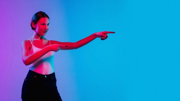 Shocked, astonished. Young caucasian woman's portrait on gradient blue-purple studio background in neon light. Concept of youth, human emotions, facial expression, sales, ad. Beautiful brunette model.