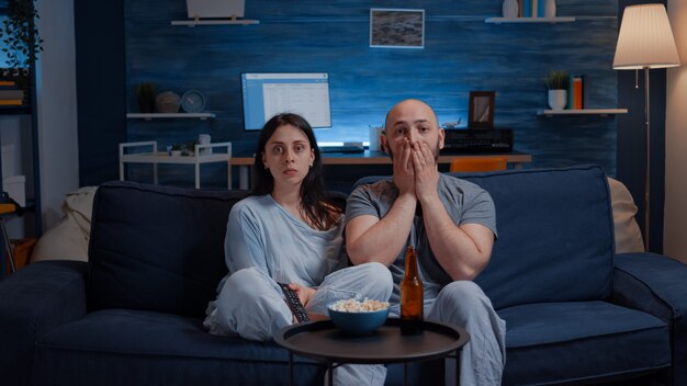 Shocked astonished young couple looking at documentary show at tv