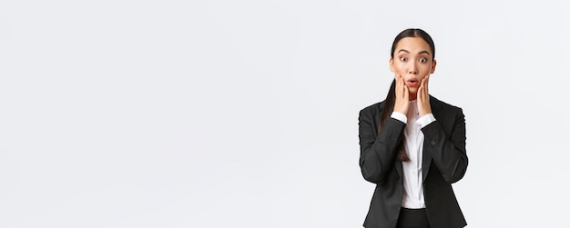 Free photo shocked and astounded asian female businesswoman hear big news saleswoman receive shocking news standing in suit looking amazed at camera signing big deal with business partners