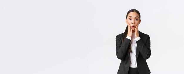 Shocked and astounded asian female businesswoman hear big news Saleswoman receive shocking news standing in suit looking amazed at camera signing big deal with business partners