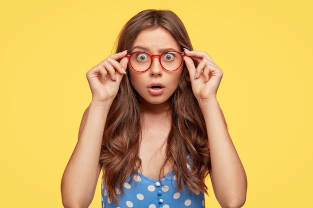 Shocked attractive young woman with glasses posing against the yellow wall