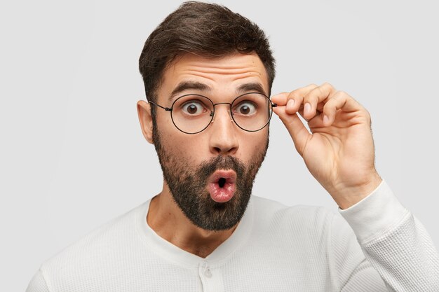 ショックを受けたひげを生やした若い男は目を飛び出し続け、眼鏡を通して見つめ、突然のニュースを不思議に思う
