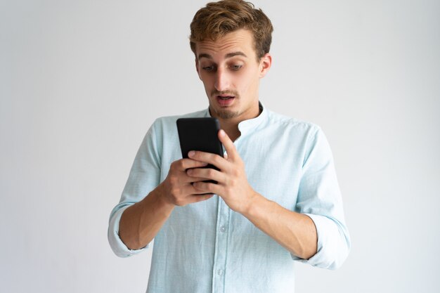 Потрясенный бородатый молодой человек, читающий интернет-новости на смартфоне.