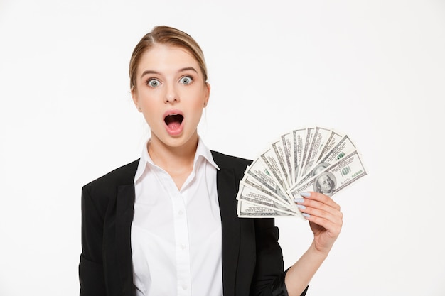 Shocked blonde business woman holding money and  with open mouth over white wall