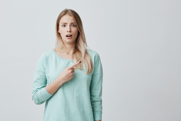 Shocked blonde woman in blue sweater with opened mouth frowning face looking