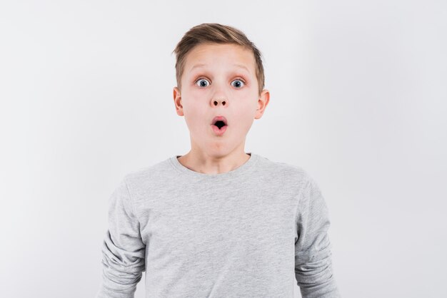 灰色の背景に対してカメラを探しているショックを受けた少年