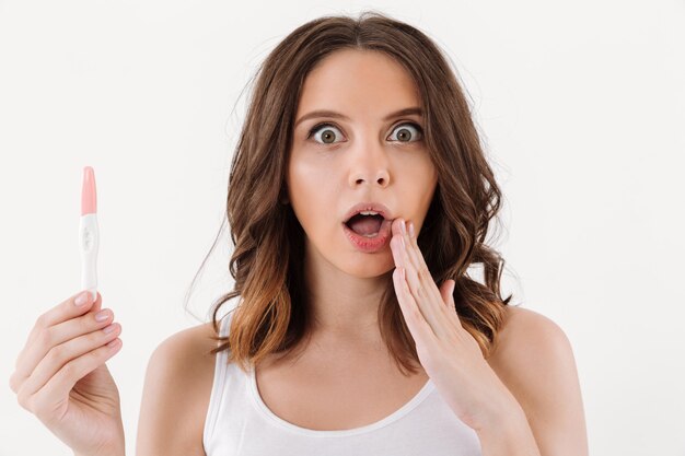 Shocked brunette woman holding positive pregnancy test