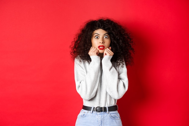 Shocked caucasian woman with curly hairstyle looking at something impressive gasping amazed checking...