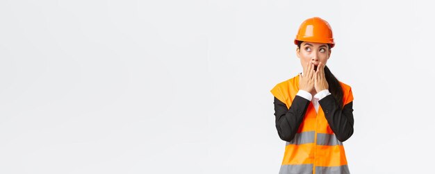 Shocked and concerned asian female engineer architect in safety helmet and reflective jacket looking