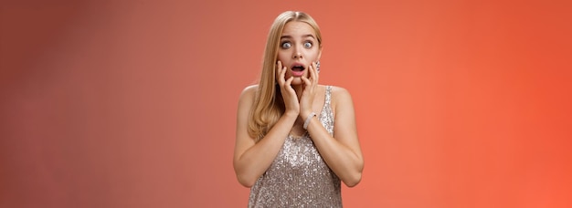 Free photo shocked concerned stunned young european blond woman in silver dres drop jaw widen eyes stunned