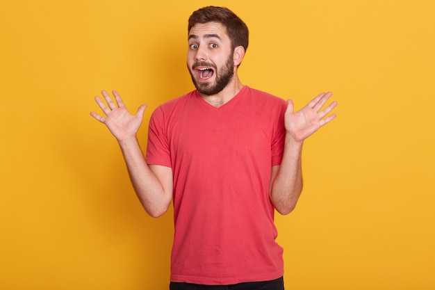 Shocked and confused caucasian bearded male model dresses casual outfit standing with spread palms and opened mouth