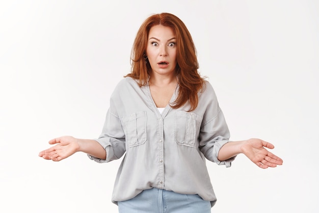 Free photo shocked confused middle-aged redhead woman spread hands sideways puzzled full disbelief shrugging wide eyes stare camera perplexed, white wall