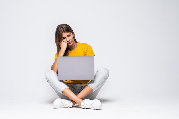 Shocked confused woman in t-shirt sitting on the floor with laptop computer on grey