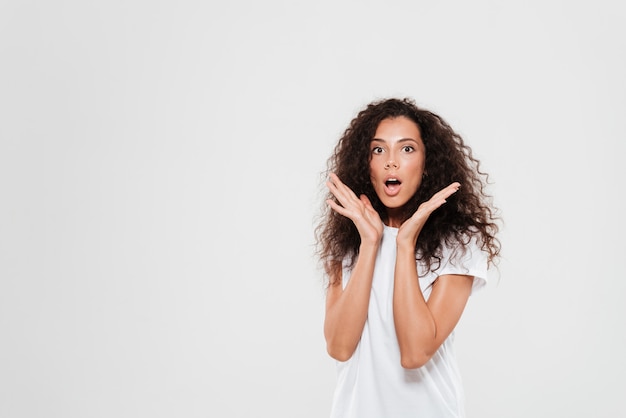 Shocked curly woman holding hands near the head