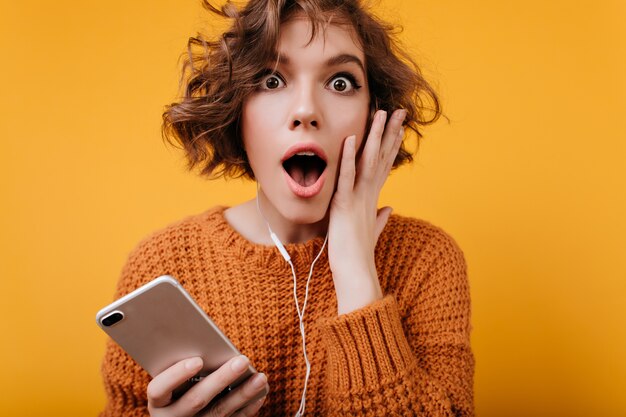 Shocked dark-eyed girl with shiny hair posing with her smartphone