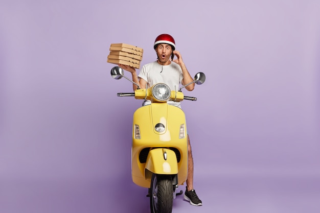 Shocked deliveryman driving scooter while holding pizza boxes