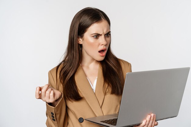 Shocked and disappointed business woman looking at laptop screen with offended frustrated face expre...