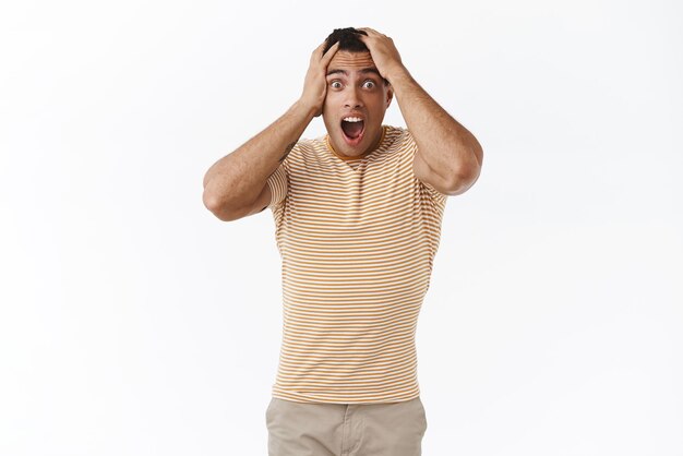 Shocked and disappointed upset young caucasian guy losing all money placing wrong bet staring startled and concerned camera grab head and shouting from failure white background