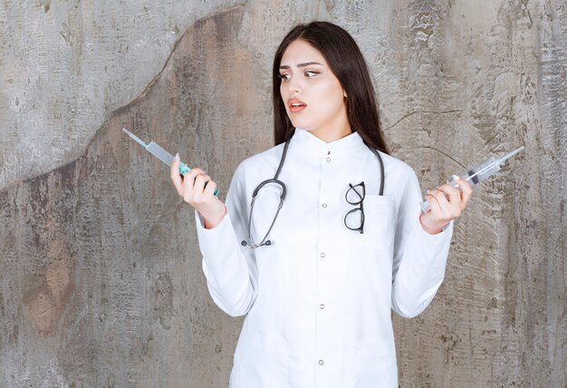 Shocked doctor holding syringes on rustic wall