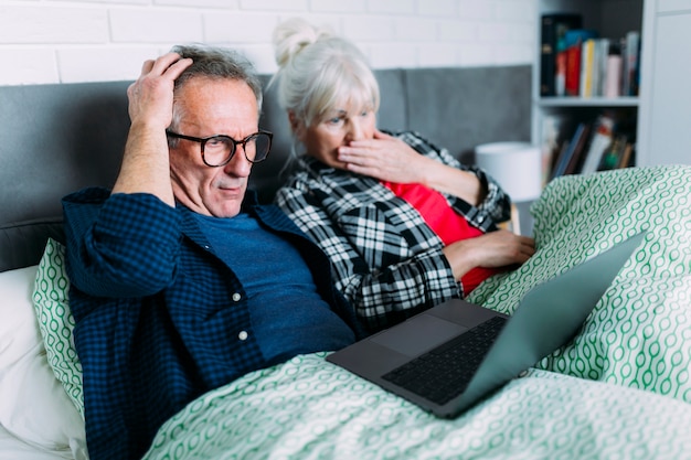 Shocked elderly couple in bed with laptop