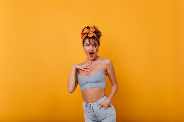 Shocked elegant woman with tanned skin standing near yellow wall