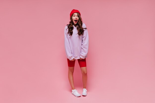 笑顔でジャンプするピンクのショートパンツで愛らしいヒスパニック系の若い女性の全身像 楽しんでいるスポーティな靴で至福のスケーターの女の子 無料の写真