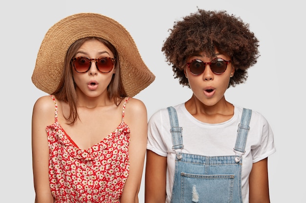 Шокированные эмоциональные женщины летом путешествуют по курорту, носят модные солнцезащитные очки и одеваются.