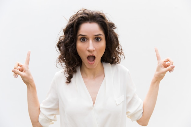 Shocked excited woman with open mouth pointing fingers up