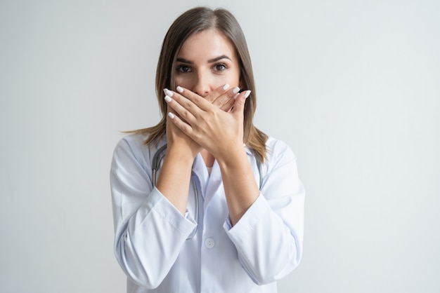 Shocked female Caucasian specialist  in lab coat covering mouth