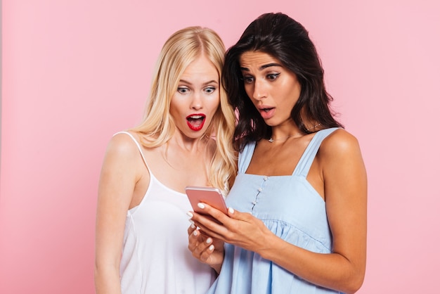 Free photo shocked female friends using smartphone isolated