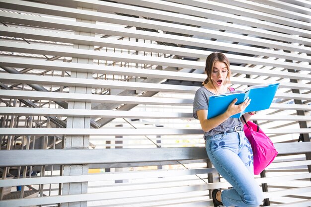 Shocked female leaning on wall and reading book