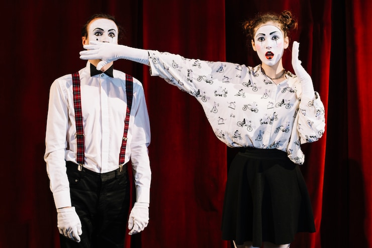 Free Photo shocked female mime artist covering male mime's mouth standing in front of curtain