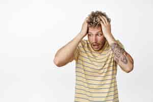 Free photo shocked and frustrated blond young man ripping his hair on head and staring aside reaction to disaster panic during terrible stressing situation white background