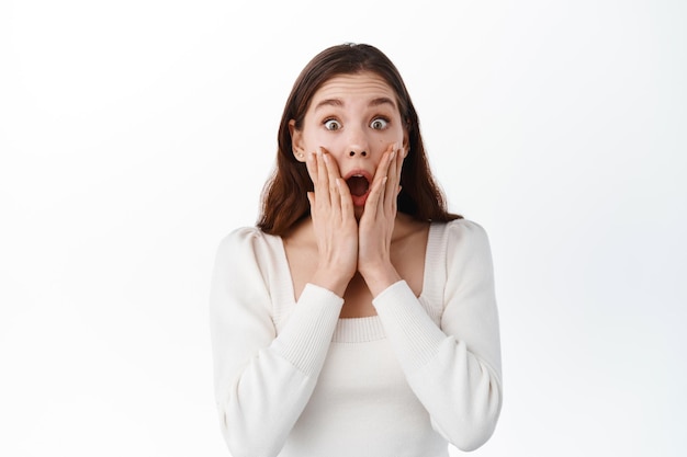 Shocked girl holding hands near opened mouth, stare fascinated with disbelief at lucky good news, stare amazed, winning and rejoicing,gasping impressed, white background