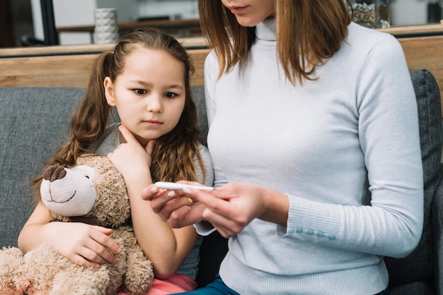 Ragazza scioccata che soffre di raffreddore e febbre guardando il termometro di sua madre