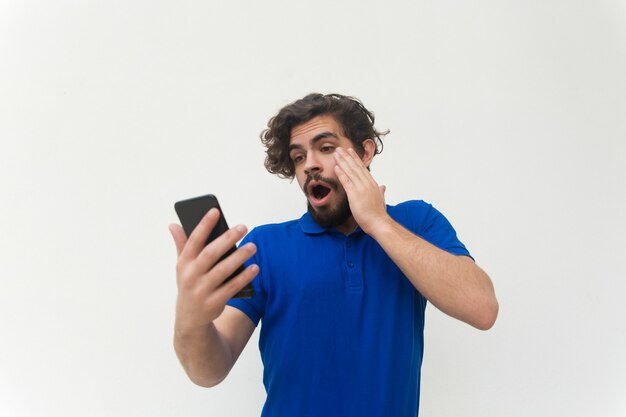 Shocked guy with smartphone reading message, staring at screen