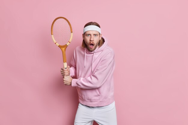 Shocked handsome male tennis player poses in ready position with racquet waits for serve