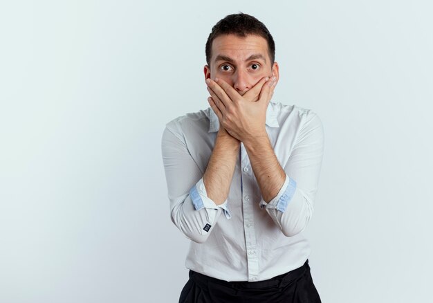 Shocked handsome man holds mouth with two hands isolated on white wall