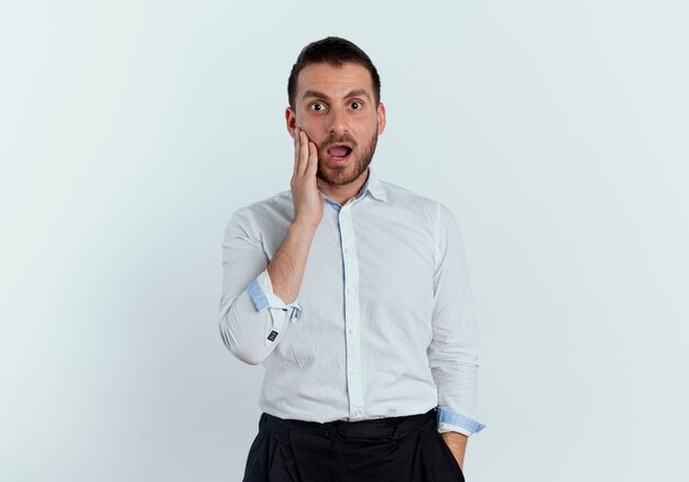 Shocked handsome man puts hand on face looking isolated on white wall